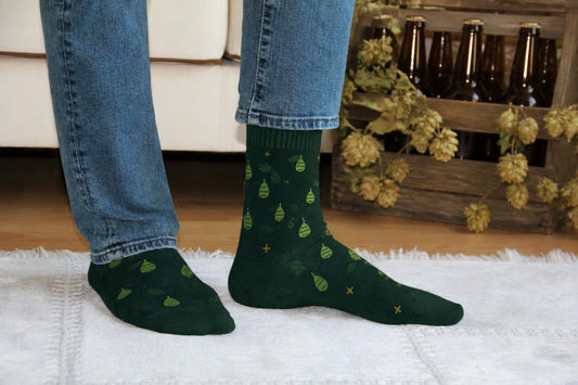 WearMoods Hop Field beer socks: forest green socks with hop cones, in front of a sofa and a crate of craft beer