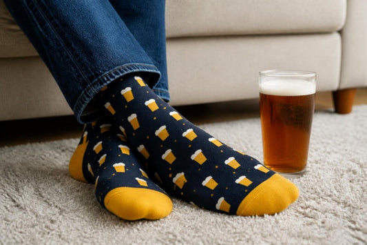 Pint Night beer socks: navy socks with mustard pint glasses, ankles crossed on a grey rug next to a pint of ale