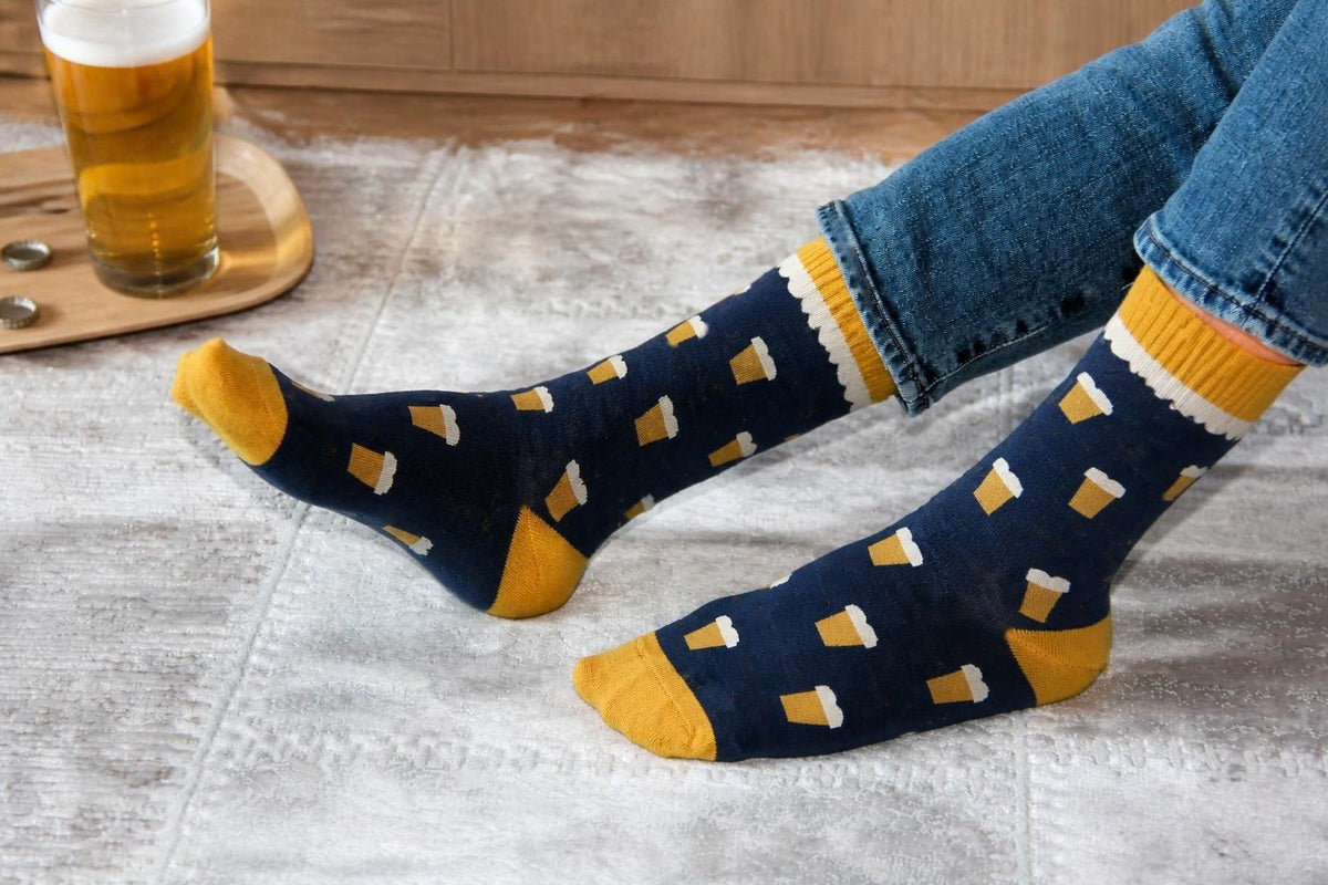WearMoods Pint Night beer socks: navy socks with foamy pints, worn on a rug next to a pint of ale